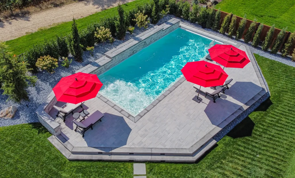 Aerial view of a pool, terrace and lawn with red umbrellas