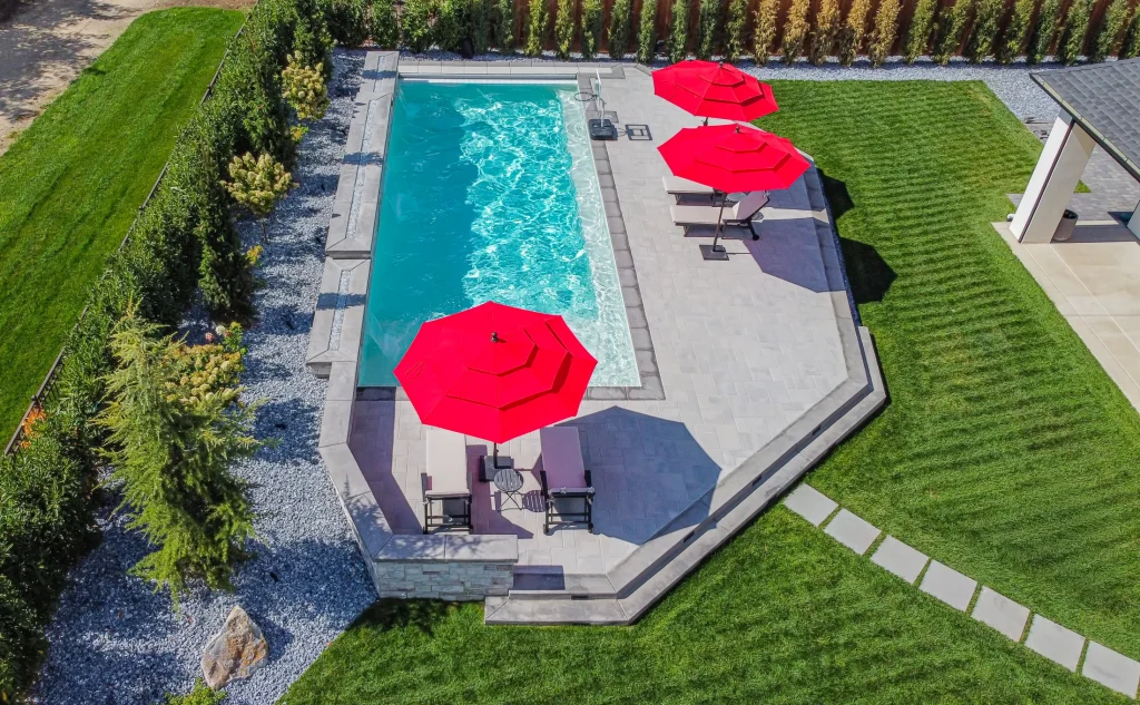 Aerial view of a pool, terrace and lawn with red umbrellas