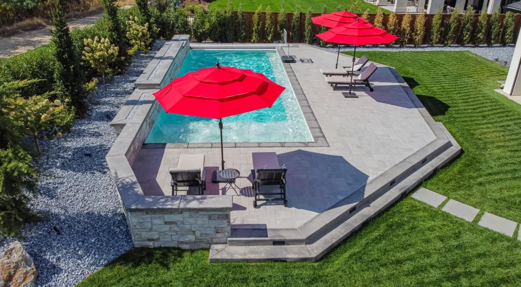 Aerial view of a pool, terrace and lawn with red umbrellas