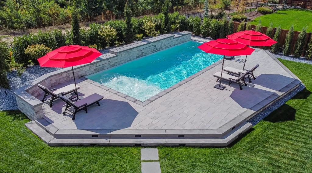 Aerial view of a pool, terrace and lawn with red umbrellas