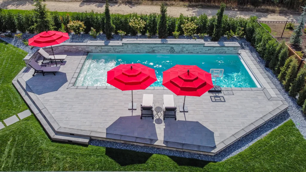 Aerial view of a pool, terrace and lawn with red umbrellas