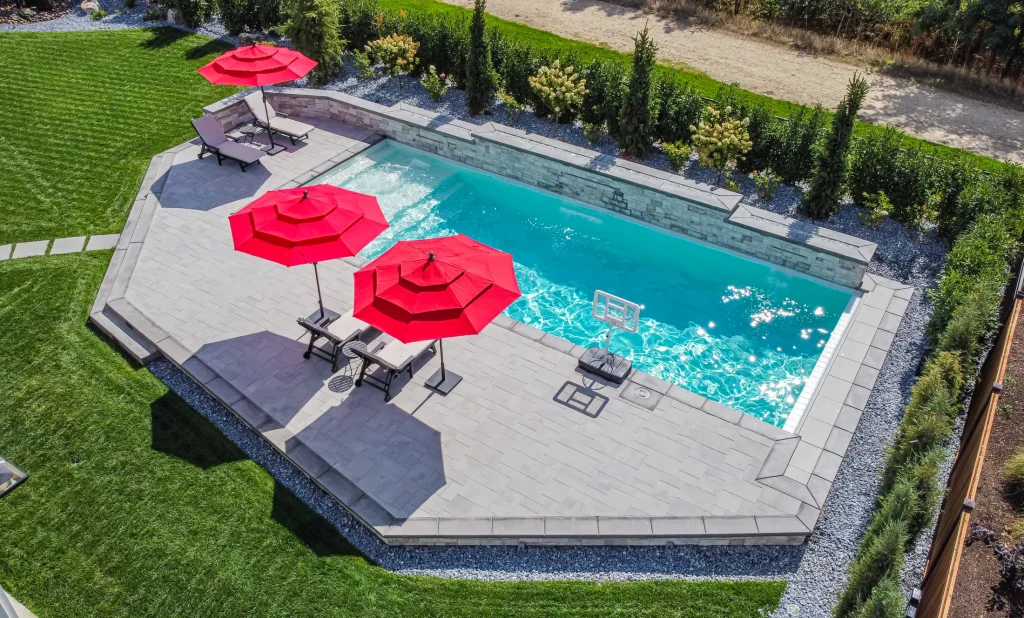 Aerial view of a pool, terrace and lawn with red umbrellas