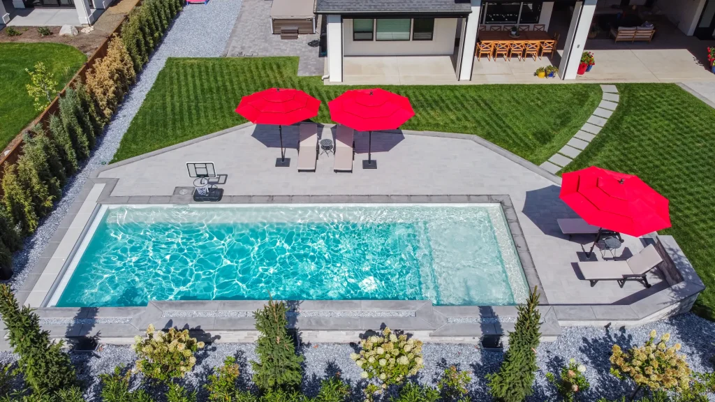 Aerial view of a pool, terrace and lawn with red umbrellas