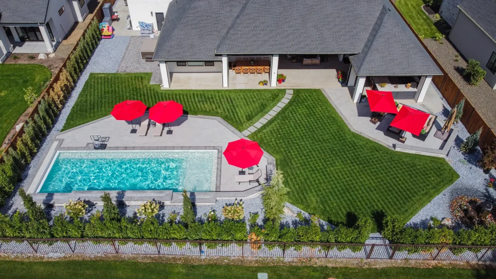 Aerial view of a pool, terrace and lawn with red umbrellas