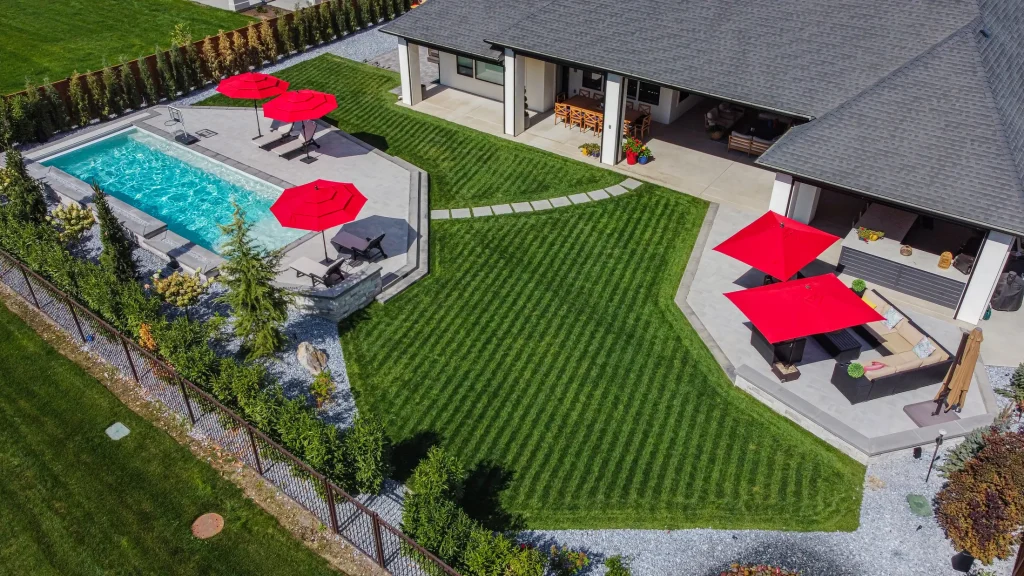Aerial view of a pool, terrace and lawn with red umbrellas