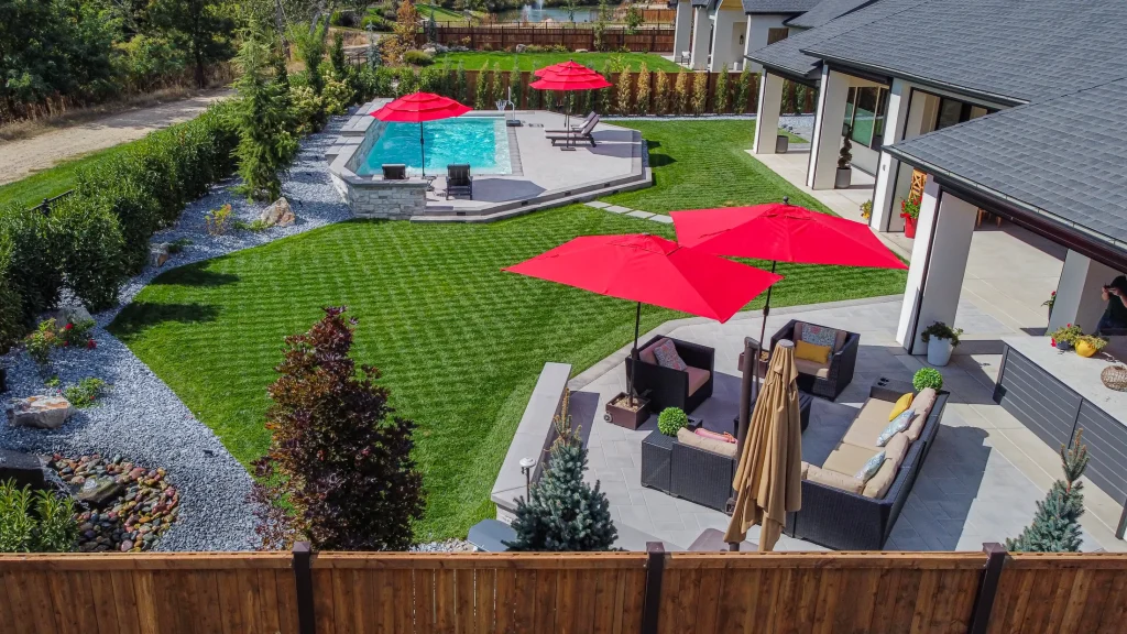 Aerial view of a pool, terrace and lawn with red umbrellas