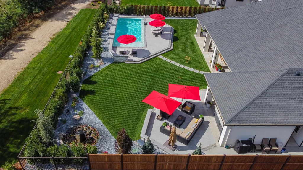Aerial view of a pool, terrace and lawn with red umbrellas